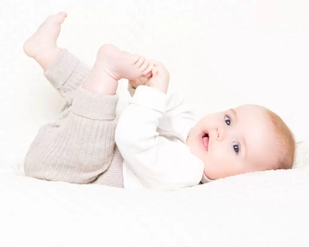 Baby Photography West Sussex a little boy laying on his back with his feet in the air on a cream blanket