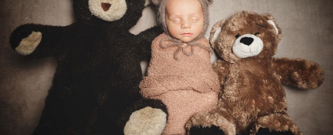 A newborn dressed as a teddy bear sitting on a shelf with two actual teddy bears