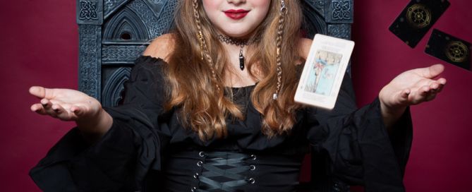 A girl dressed as a fortune teller throwing tarot cards into the air while sitting on a skull throne