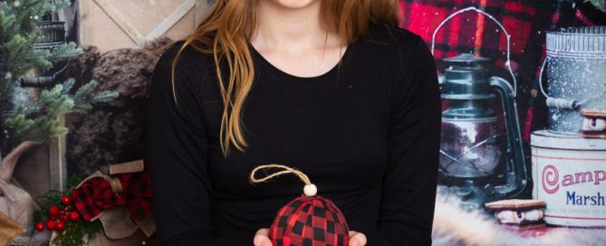 a young girl holds a christmas bauble as she poses for a plaid themed christmas photo