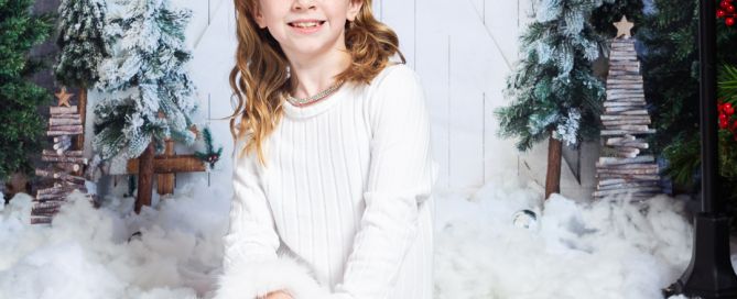 a little girl in a pile of snow at a Christmas Themed photo shoot in a white dress