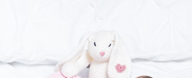 a sleeping newborn baby girl wrapped in pink and her new rabbit toy