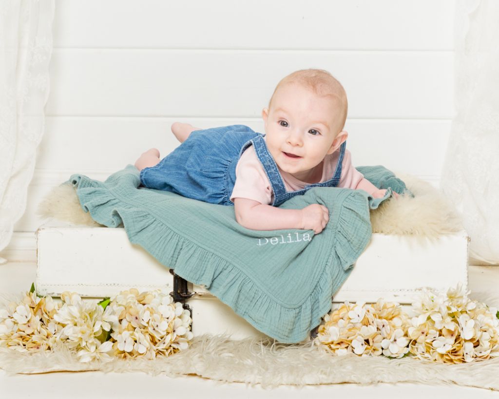 a little girl lies on her personalised blanket on a vintage suitcase at a photo shoot