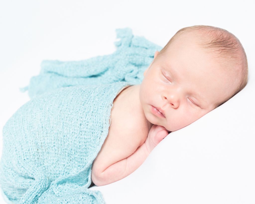 a newborn sleeping on their tummy with a light blue wrap across them