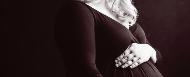 Expectant mother posing in a dark, moody studio setting, highlighting her baby bump.