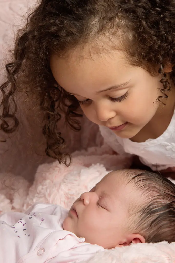 a little girl leans over her new sister at a newborn photo shoot