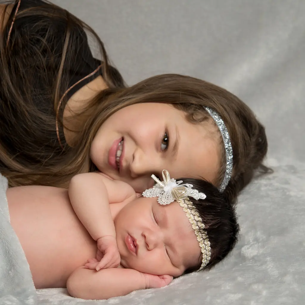 A little girl lies down behind her sister at a newborn photo shoot