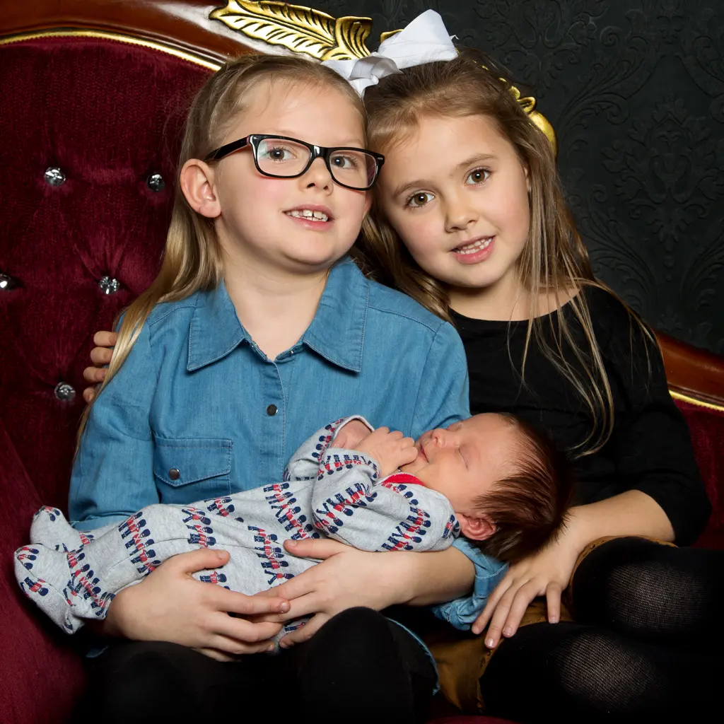 Two sisters hold their new baby brother