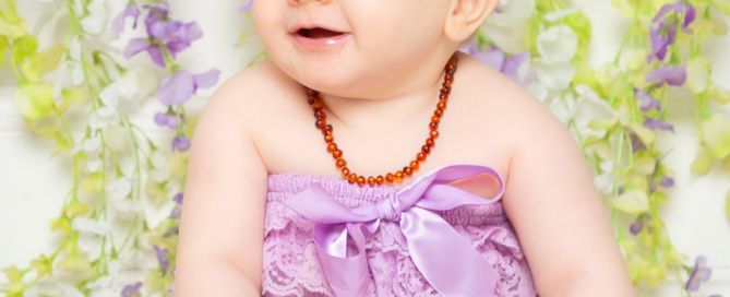 A baby poses in a lilac frilly outfit in a photographic studio in front of a mauve and white flower wall backdrop.