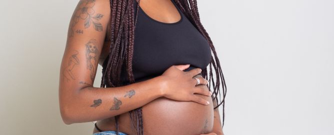 a pregnant woman kneels down looking at her baby bump at a professional photo shoot
