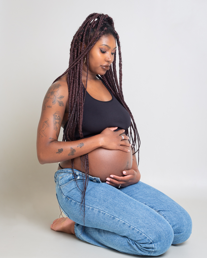 a pregnant woman kneels down looking at her baby bump at a professional photo shoot