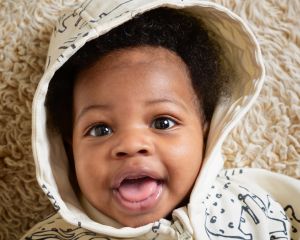 a baby looks up at the camera in a hooded jumper and smiles