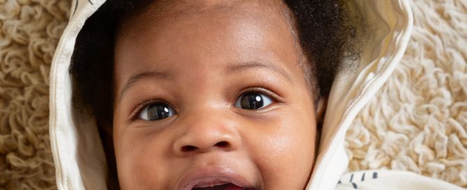 a baby looks up at the camera in a hooded jumper and smiles