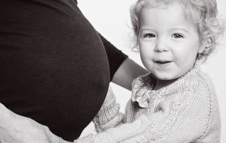 A little girl snuggles up to her mums pregnant belly in a black and white image