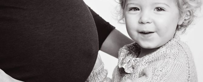 A little girl snuggles up to her mums pregnant belly in a black and white image