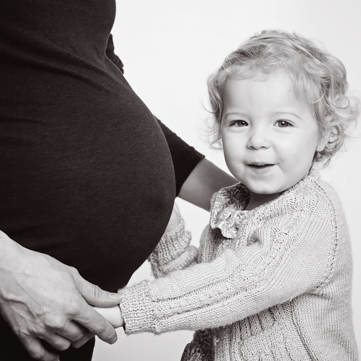 A little girl snuggles up to her mums pregnant belly in a black and white image