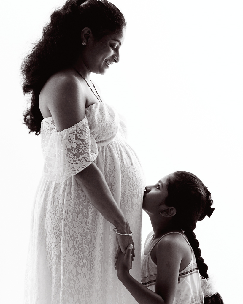 A little girl snuggles up to her mums pregnant belly in a black and white image