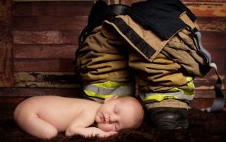 A newborn sleeping next to a pair of firefighter trousers