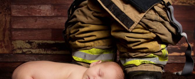 A newborn sleeping next to a pair of firefighter trousers