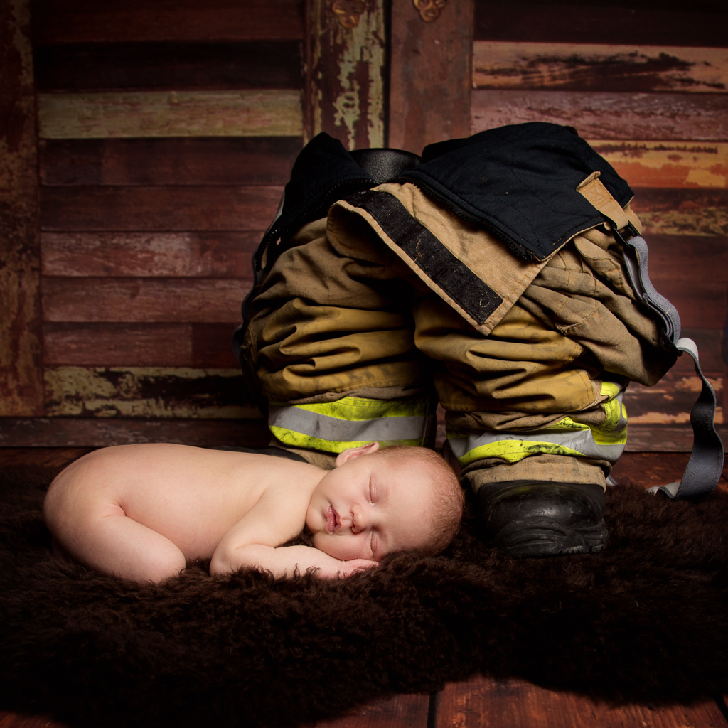 A newborn sleeping next to a pair of firefighter trousers