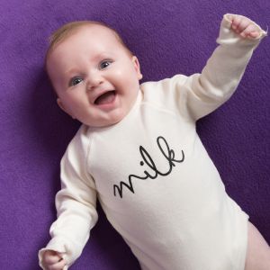 a smiling baby in a romper that says milk against a purple backdrop
