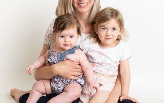 a mum sits on the floor at the studio with her two daughters on her lap