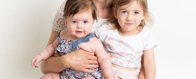 a mum sits on the floor at the studio with her two daughters on her lap