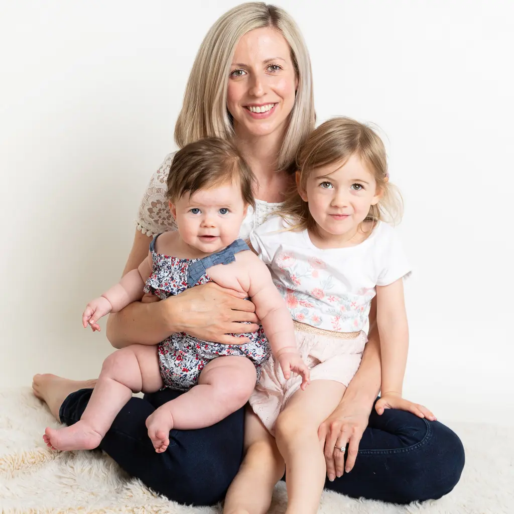 a mum sits on the floor at the studio with her two daughters on her lap