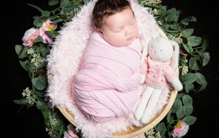 a newborn wrapped in pink sleeping in a bowl with a stuffed bunny toy