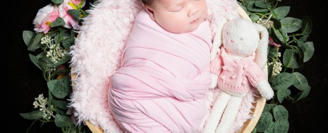 a newborn wrapped in pink sleeping in a bowl with a stuffed bunny toy