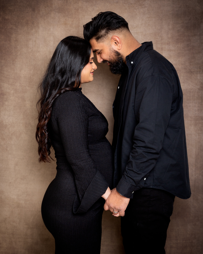 A pregnant woman holds hands with her husband as they look together down to the baby bump