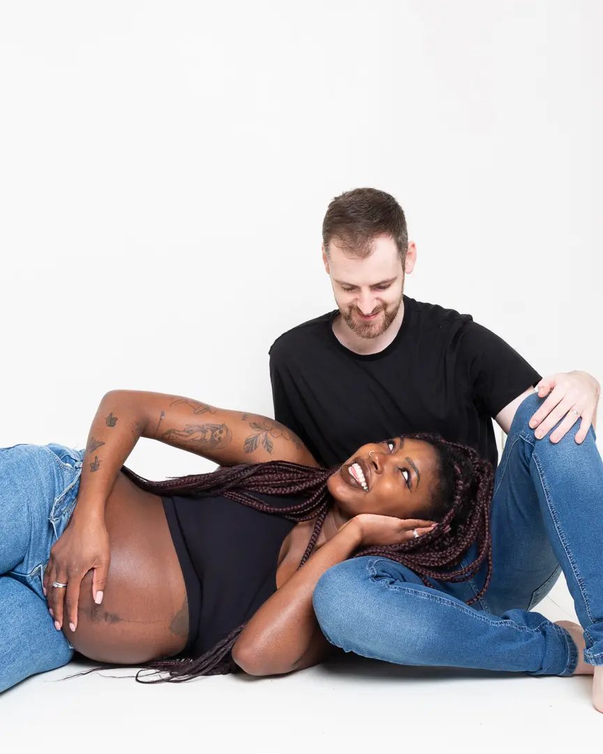 A couple,, with the woman being pregnant, look at each other while sitting on the floor