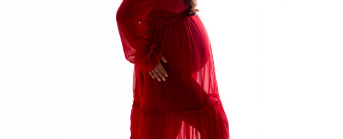 A pregnant woman poses in a flowing red dress