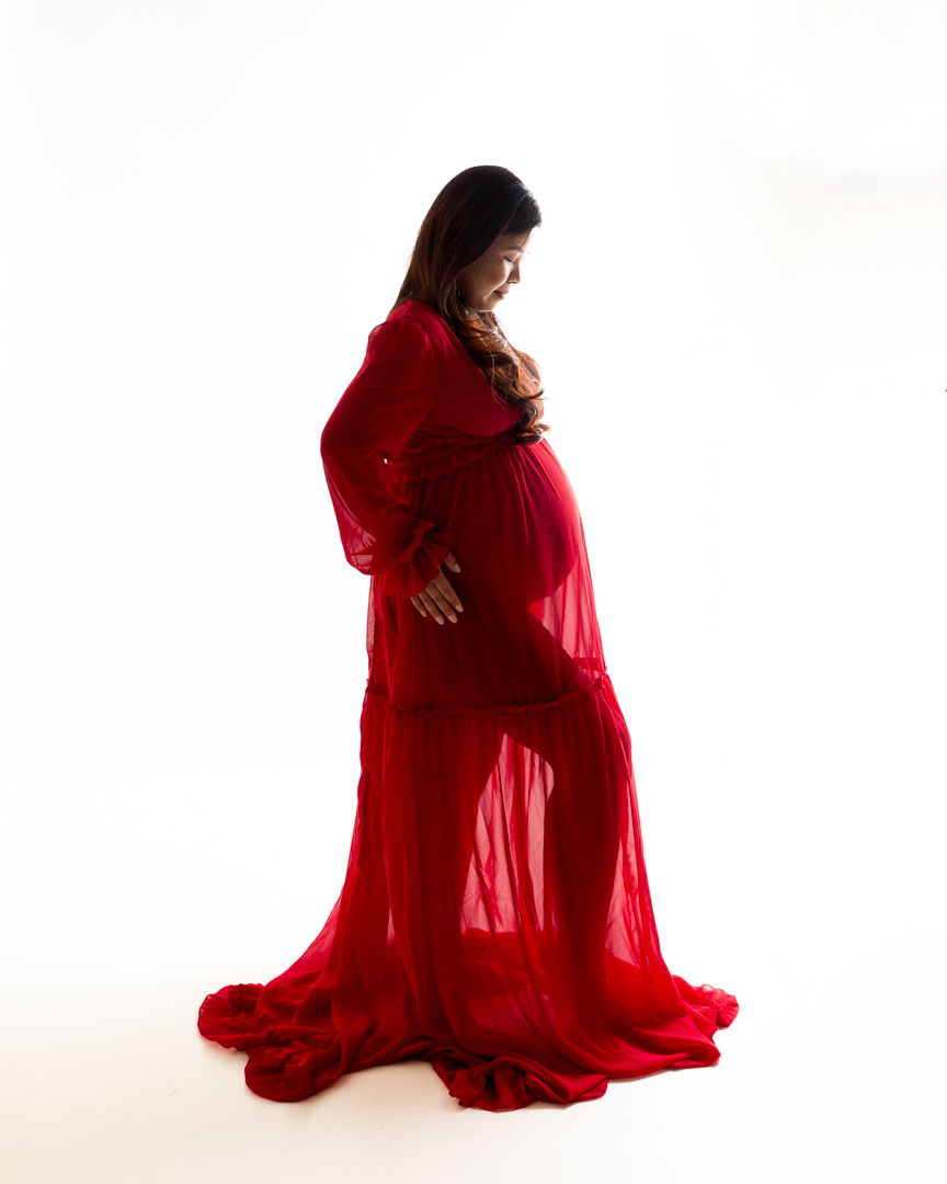 A pregnant woman poses in a flowing red dress