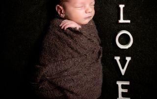 a newborn swaddled in a brown wrap next to letters spelling LOVE