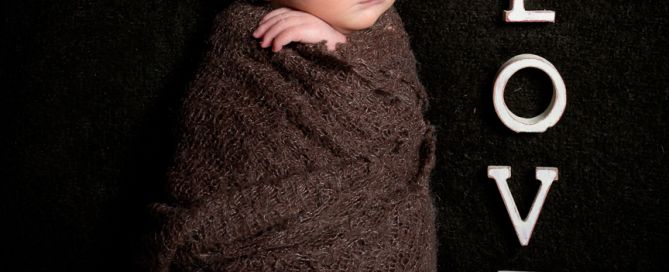 a newborn swaddled in a brown wrap next to letters spelling LOVE