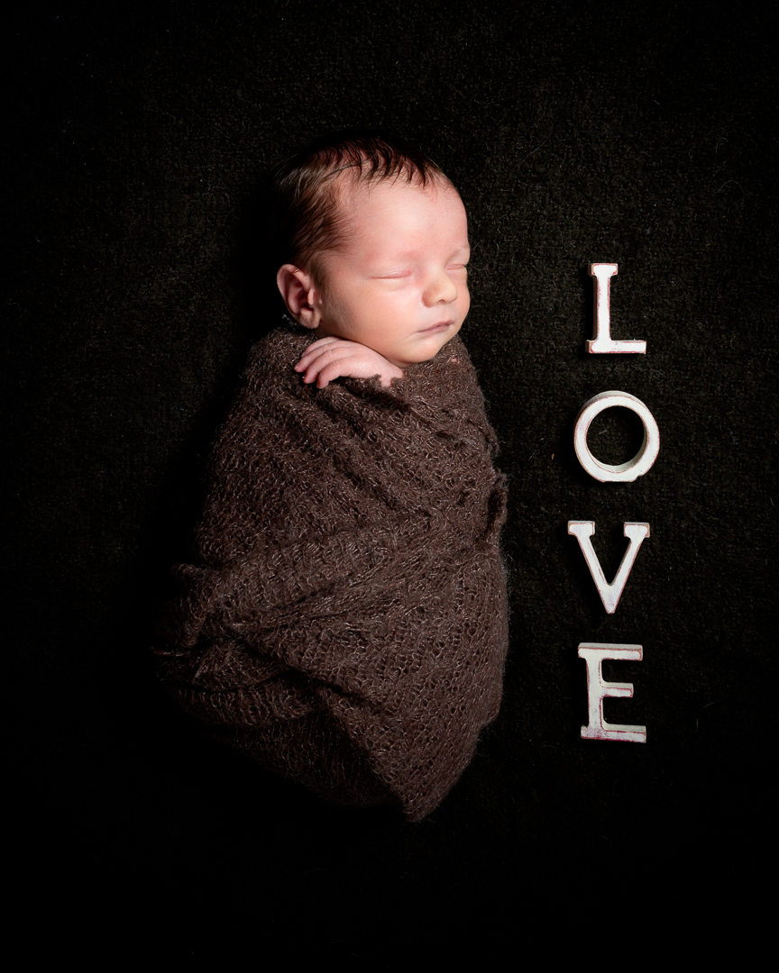 a newborn swaddled in a brown wrap next to letters spelling LOVE