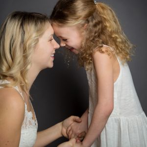 a mum and daughter dressed in white pose together touching noses and laughing