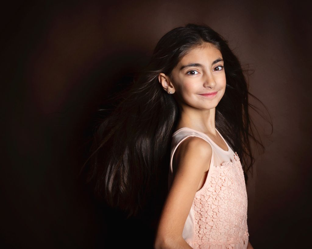 a girl in a peach dress photographed with her hair flying against a brown background