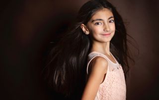 a girl in a peach dress photographed with her hair flying against a brown background