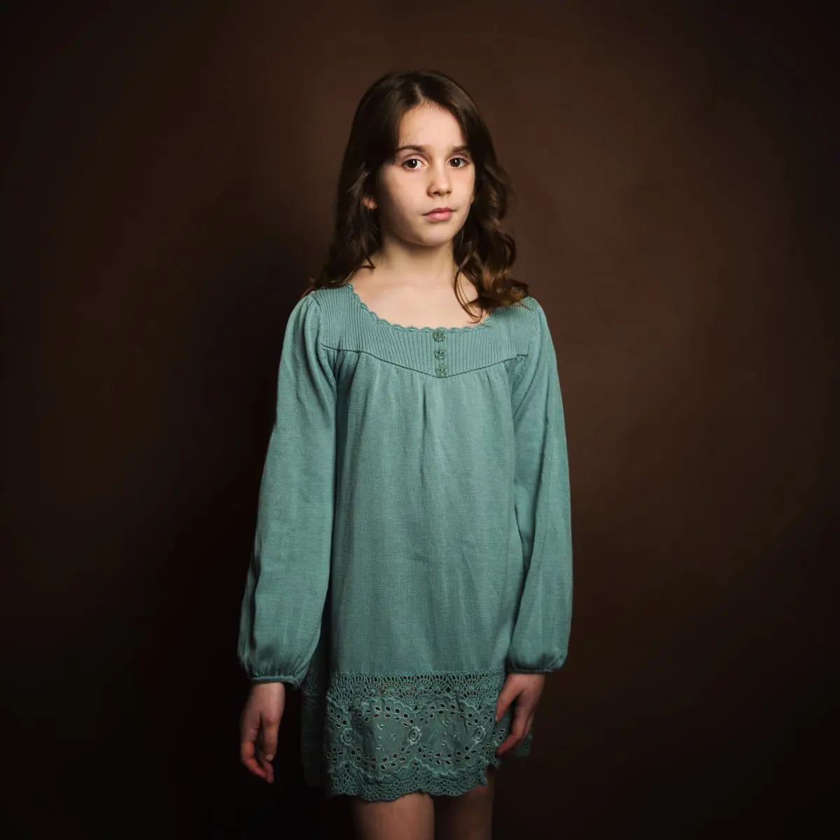 a dark haired girl poses in a blue dress against a brown backdrop for a fine art child's portrait