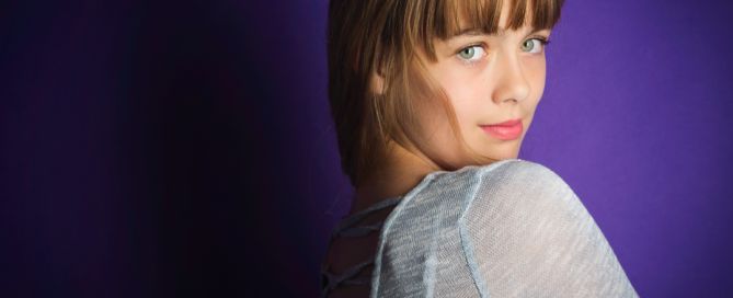 a girl poses looking over her should against a purple backdrop at a fine art portrait shoot