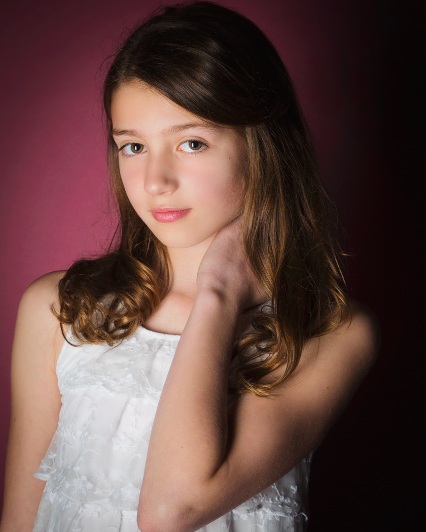 a girl poses in a lace top against a rose colour background