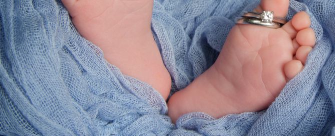 a little pair of newborn feet wrapped in blue with their parents wedding rings balanced on their toes