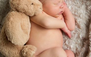 a newborn curled up asleep with his brand new teddy bear