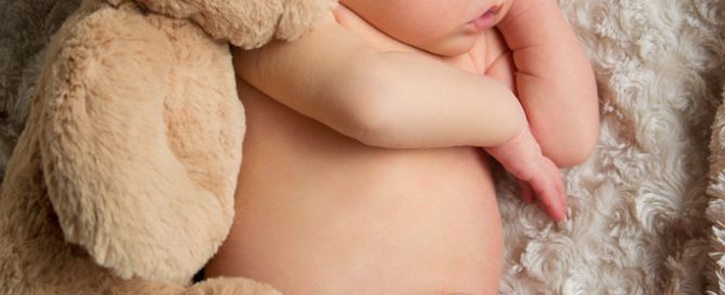 a newborn curled up asleep with his brand new teddy bear
