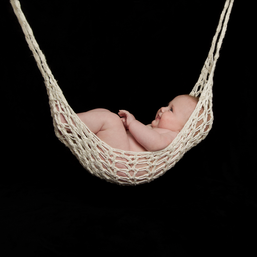 a baby in a string hammock against a black background