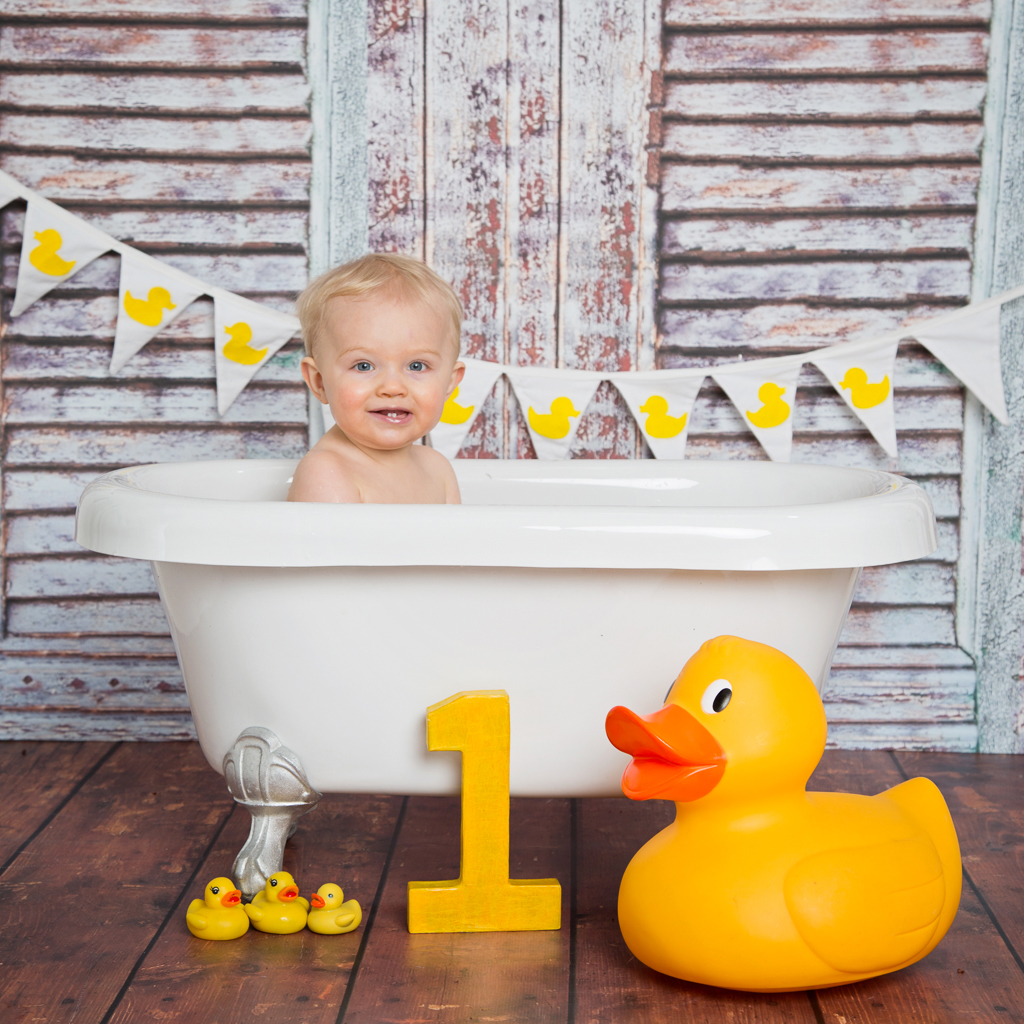 a little boy in a tin tub with a cream background and a giant duck
