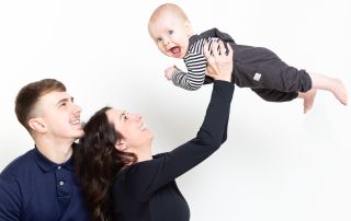 a mum and dad fly their son into the air at a portrait photo shoot