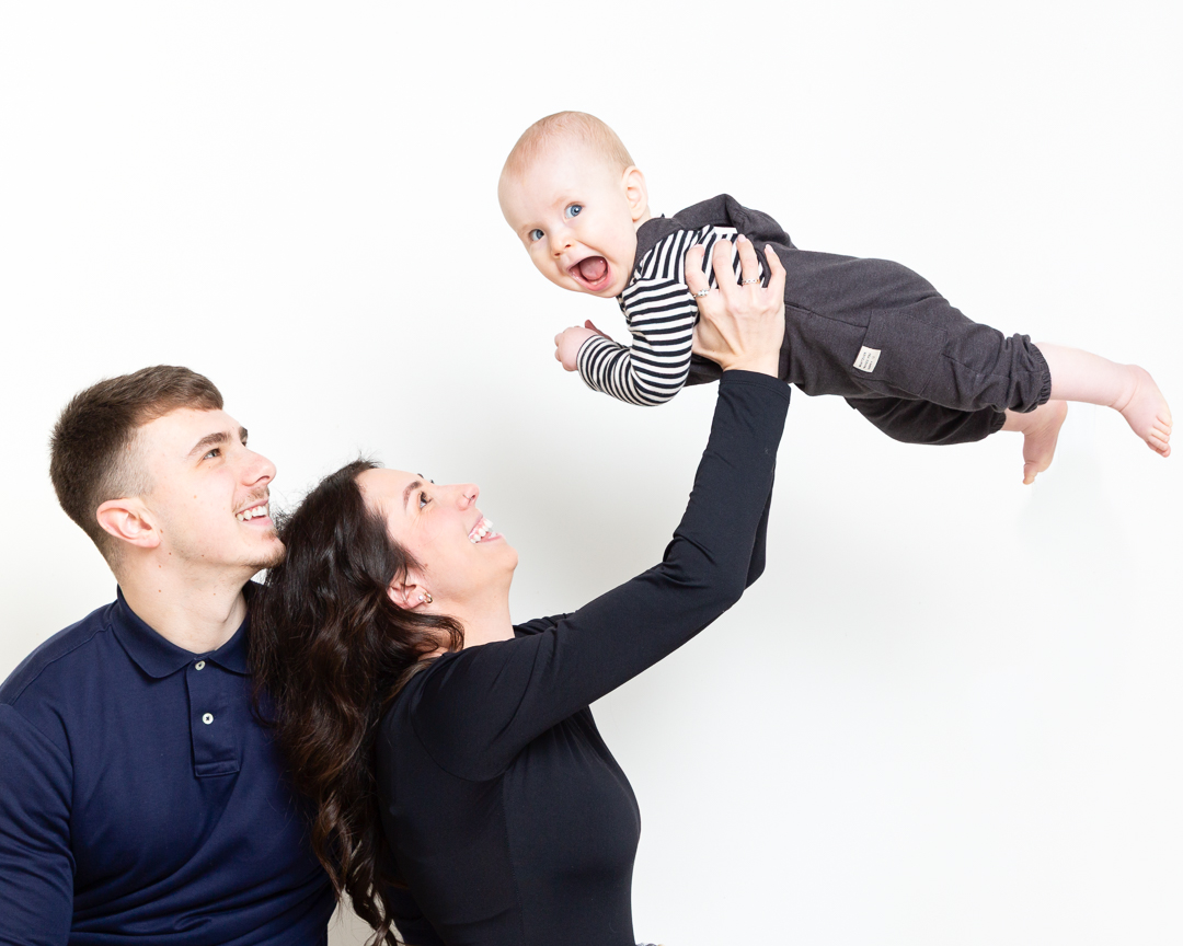 a mum and dad fly their son into the air at a portrait photo shoot